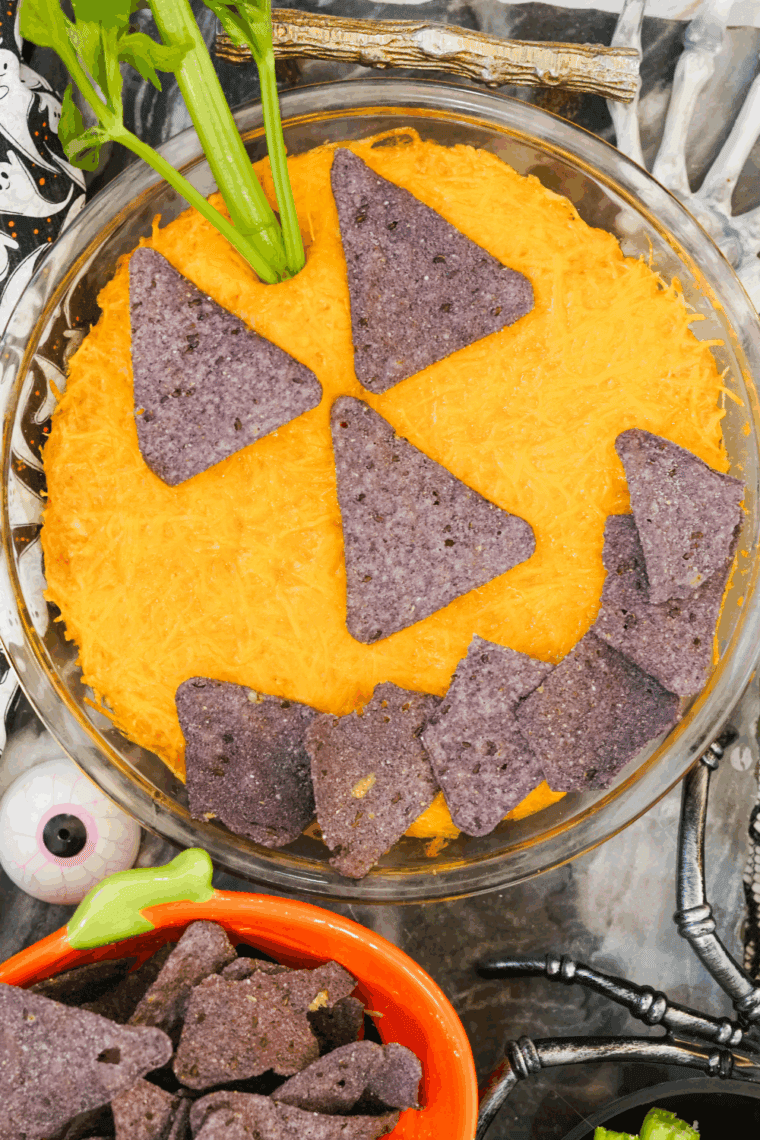 Halloween Boo-falo Wing Dip baked and decorated with celery “stem” and tortilla chip pumpkin face, ready to serve.