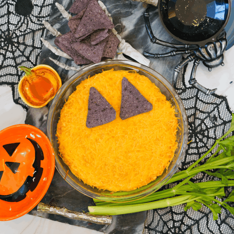 Festive Halloween Boo-falo Wing Dip baked and topped with celery “stem” and tortilla chip pumpkin face, ready to serve.