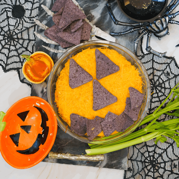 Halloween Boo-falo Wing Dip in a baking dish, decorated with celery “stem” and tortilla chip pumpkin face.