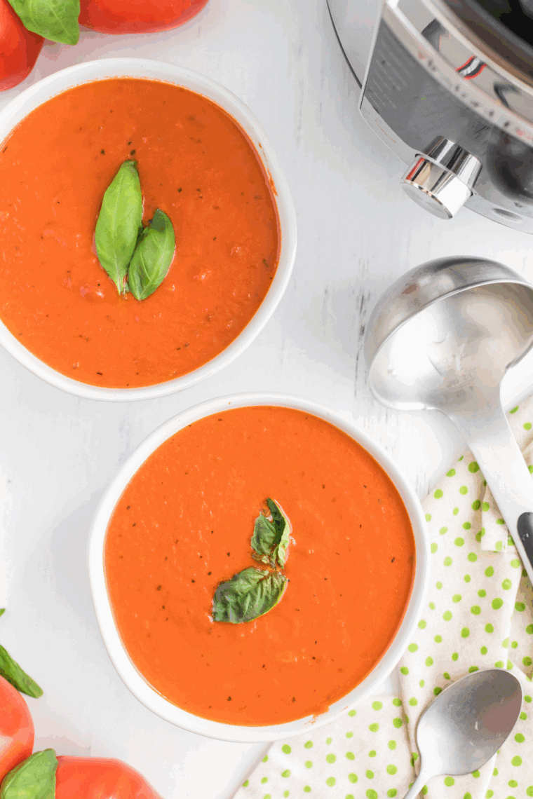 Bowl of creamy Instant Pot Madeleine Tomato Basil Soup garnished with fresh basil and served with crusty bread.