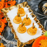 Mini pumpkin-shaped cheese balls coated in crushed crackers with pretzel stems and parsley leaves, served on a fall appetizer platter.