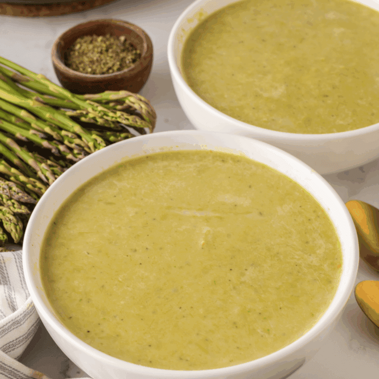 Bowl of creamy Barefoot Contessa Cream of Asparagus Soup garnished with fresh herbs.