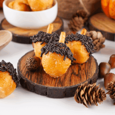 Plate of soft, spiced acorn-shaped donut holes decorated with chocolate and crushed nuts.