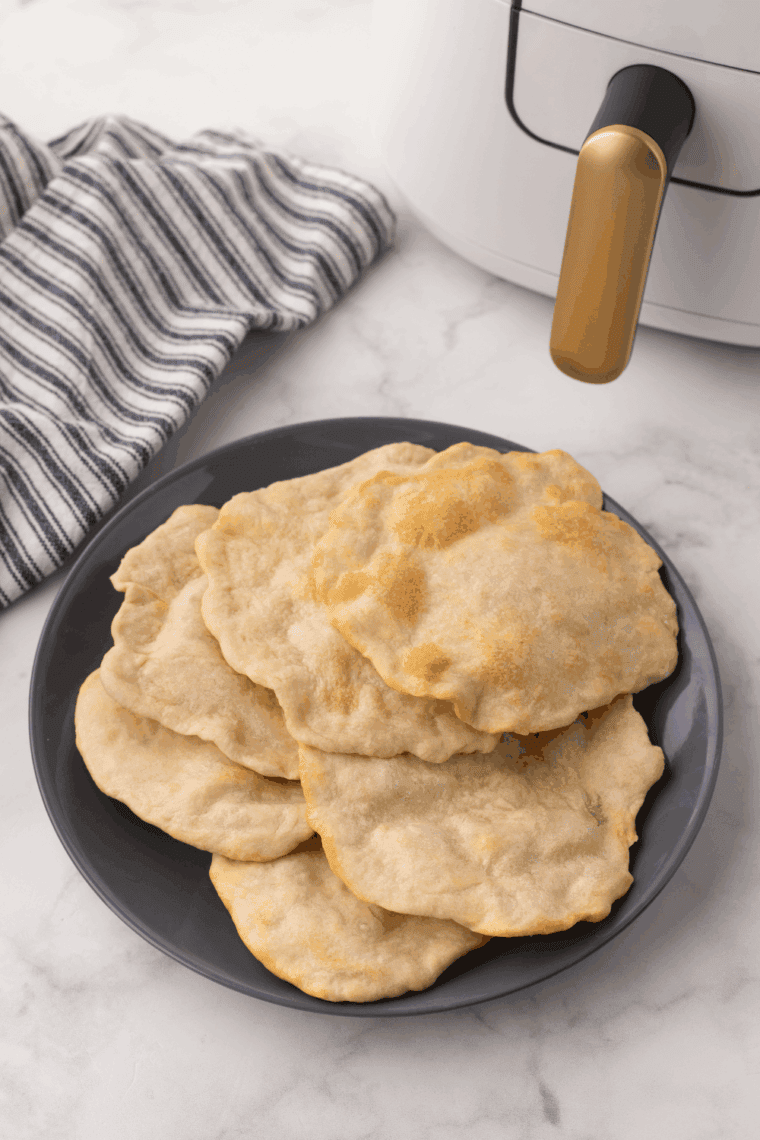 Plate of Easy Air Fryer Homemade Flour Tortillas on kitchen table, near air fryer basket.