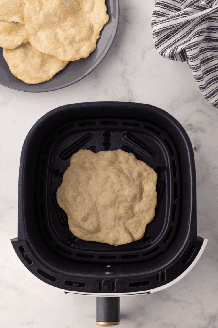 Stack of golden, freshly made air fryer homemade flour tortillas on a kitchen towel.