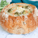 Creamy Copycat Subway Broccoli and Cheese Soup in a white bowl topped with shredded cheddar and fresh broccoli florets.