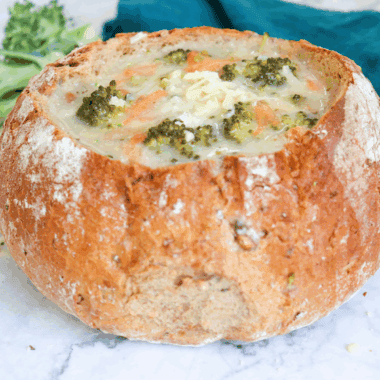Creamy Copycat Subway Broccoli and Cheese Soup in a white bowl topped with shredded cheddar and fresh broccoli florets.