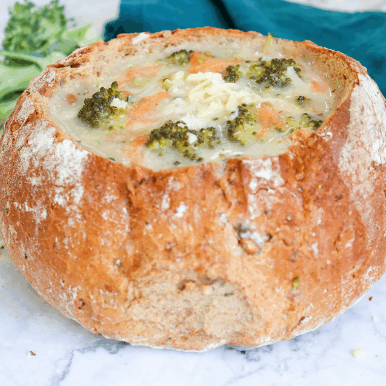 Creamy Copycat Subway Broccoli and Cheese Soup in a white bowl topped with shredded cheddar and fresh broccoli florets.