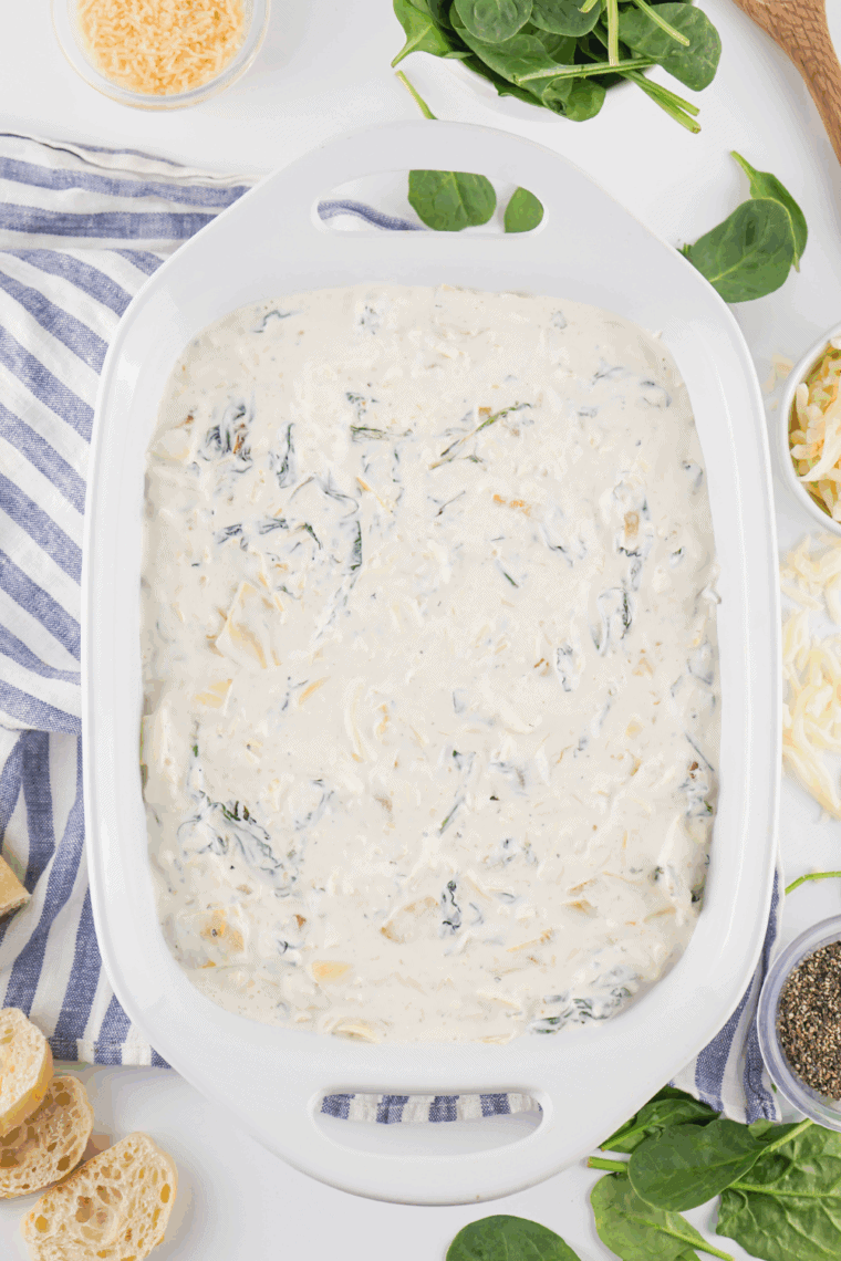 Bowl of spinach dip mixture with chopped spinach, water chestnuts, and green onions being stirred together.
