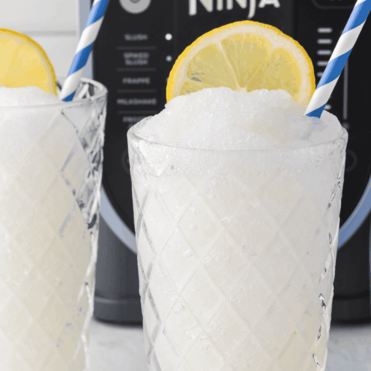 Glass of frosty Ninja Slushi Frosted Lemonade garnished with a lemon slice.