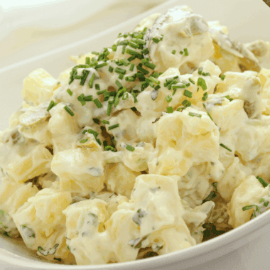 Bowl of creamy French Potato Salad by Barefoot Contessa garnished with fresh parsley and chives.