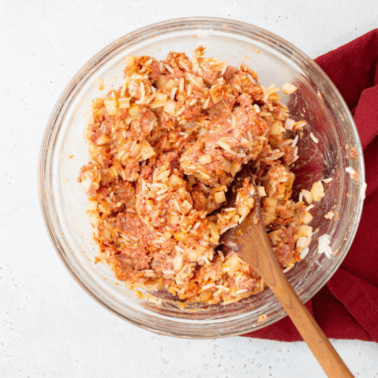 Cooking onions and garlic in olive oil, then mixing with raw ground beef, rice, egg, salt, and pepper to create the filling for stuffed cabbage rolls.