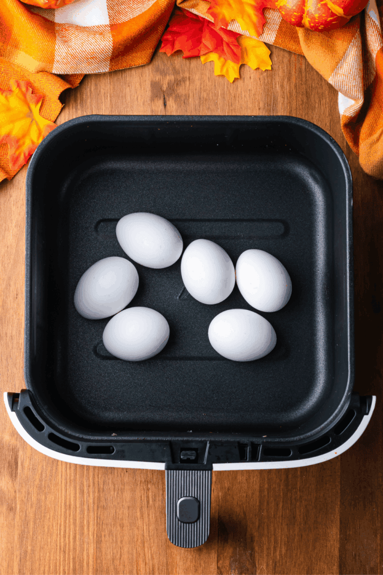 Six large eggs in an air fryer basket before hard boiling
