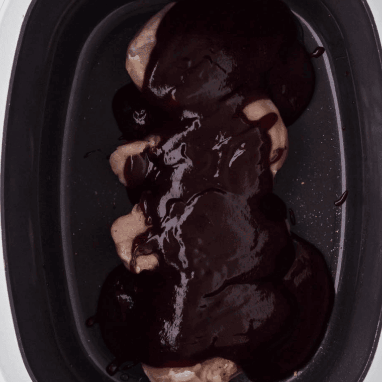 Pouring rich BBQ sauce mixture over chicken breasts in the Ninja Foodi, coating each piece evenly for slow cooking.