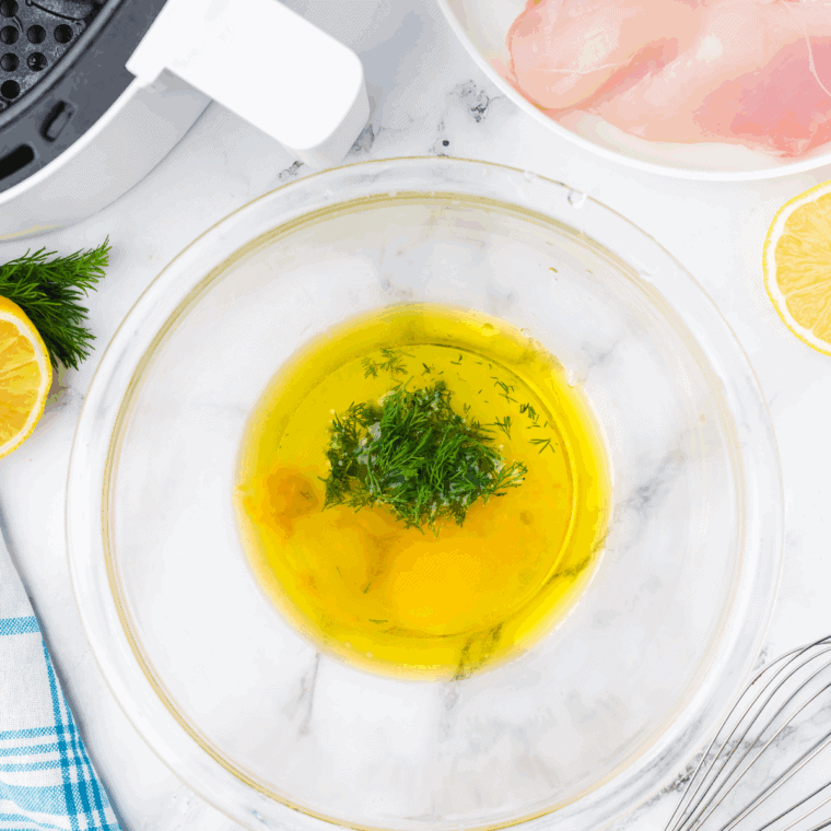 Bowl of lemon garlic herb marinade with fresh herbs and garlic cloves ready for chicken