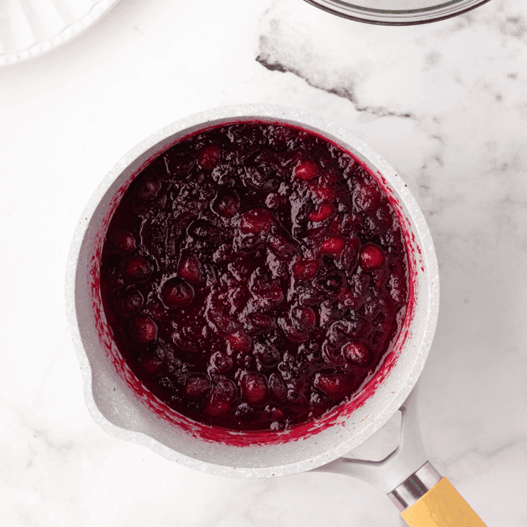 Cranberry mixture simmering in a saucepan, thickening and bursting.