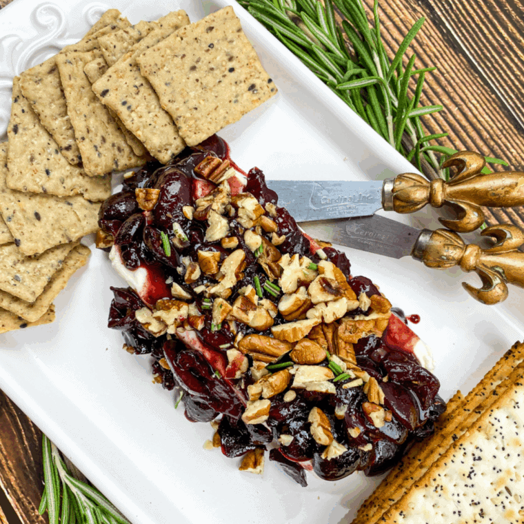 Creamy block of cream cheese topped with glossy warm cherry sauce and sprinkled with chopped pecans.