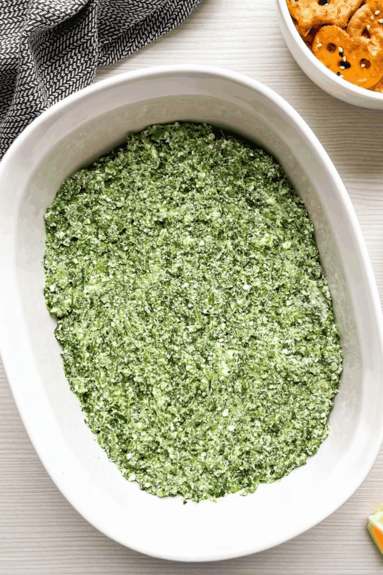 Transferring creamy spinach mixture into a casserole dish and topping with feta.