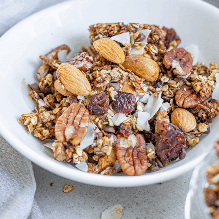 Homemade First Watch granola with oats, almonds, sunflower seeds, and golden clusters of baked sweetness in a glass jar.