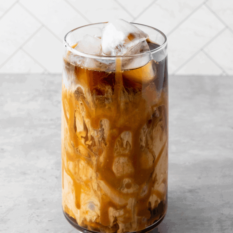 Milk and sweetener being stirred into iced coffee.