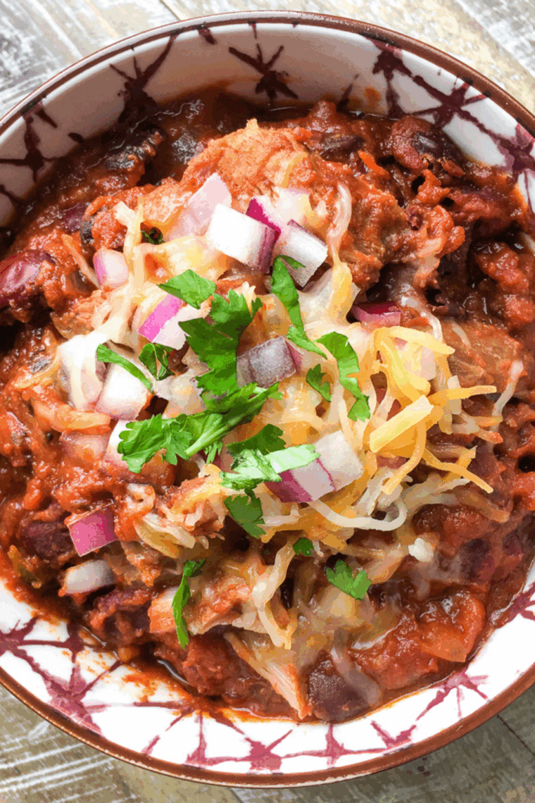 Bowl of Easy Slow Cooker Pulled Pork Chili with beans, topped with chopped onions and cilantro.