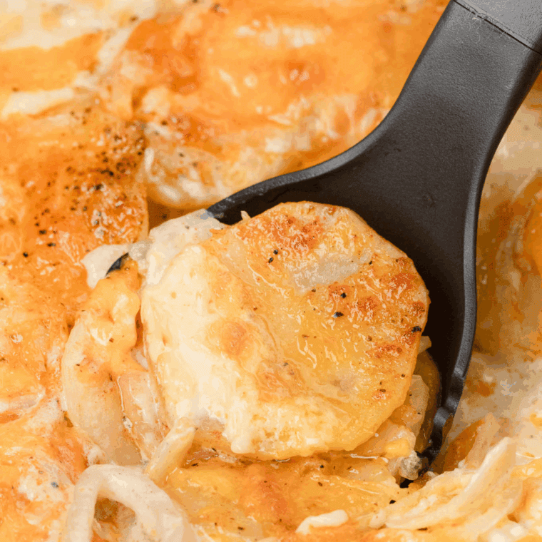 Creamy, cheesy scalloped potatoes baked until golden, visible in a slow cooker insert or transferred to a serving dish.