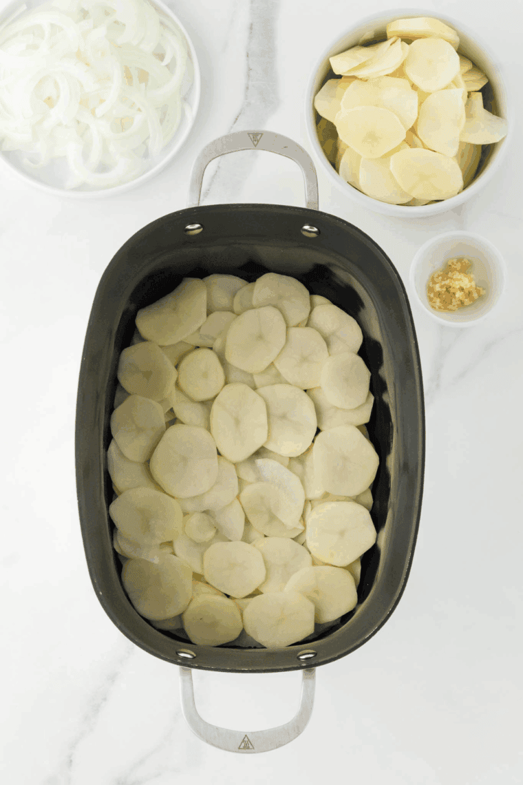 Thinly sliced potatoes arranged in the bottom of slow cooker