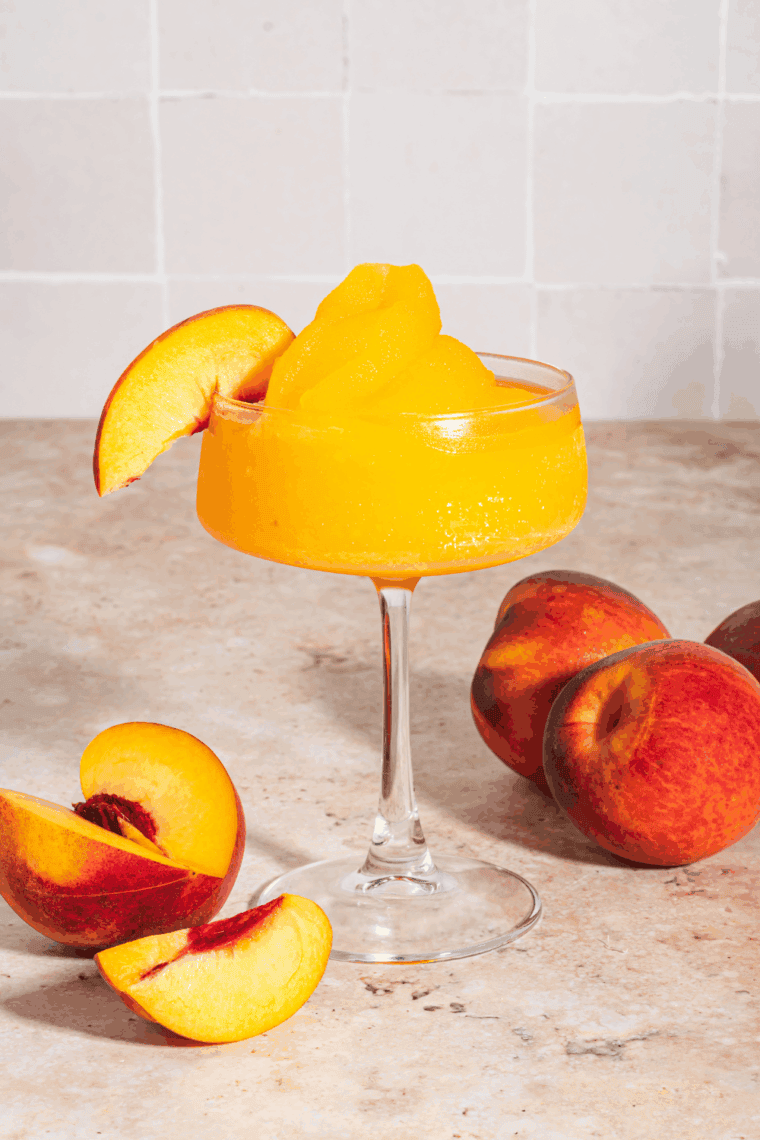 Frozen peach bellini slushi in a glass with a straw, made using a Ninja Slushi.
