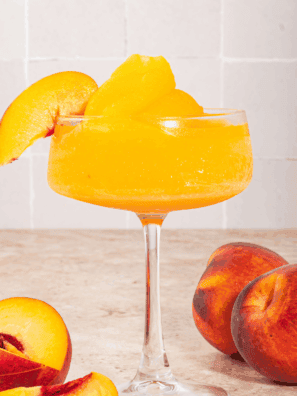 Frozen peach bellini slushi served in a glass with a straw, made using a Ninja Slushi.