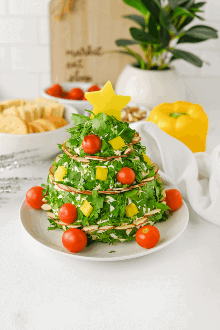 Christmas tree shaped cheese ball decorated with herbs and red peppers on serving board