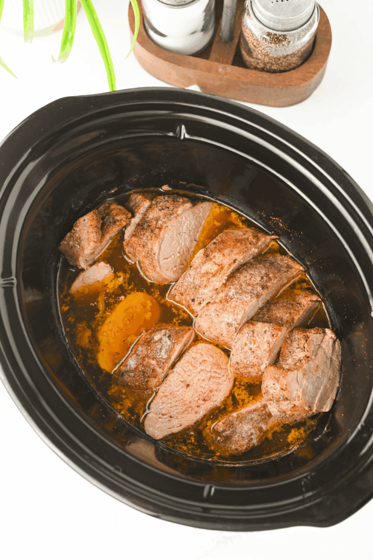 Juicy slow cooker pork tenderloin sliced into medallions and topped with garlic herb gravy on a white plate