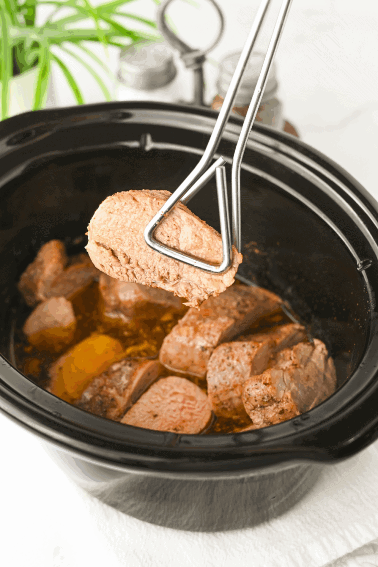 Close-up of tender, juicy slow cooker pork tenderloin medallions with gravy spooned over the top