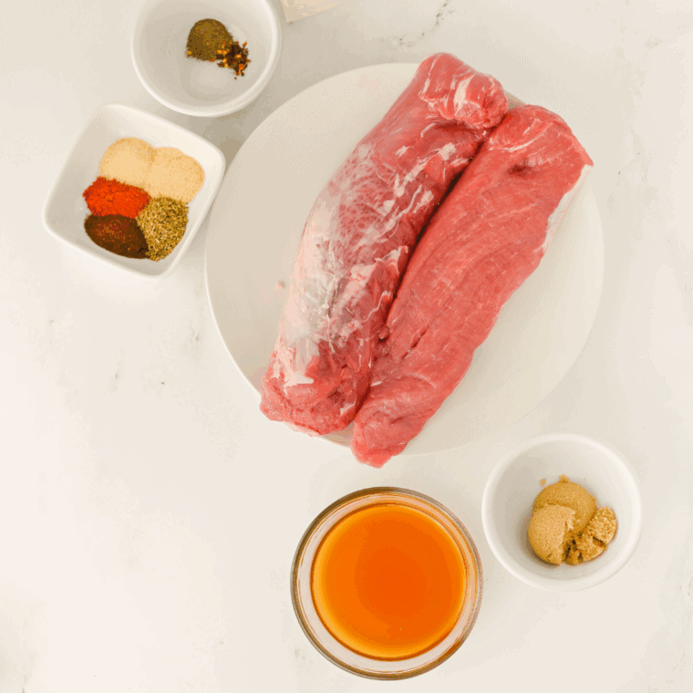 Ingredients for slow cooker pork tenderloin including pork, broth, garlic, herbs, honey, and Dijon on a countertop