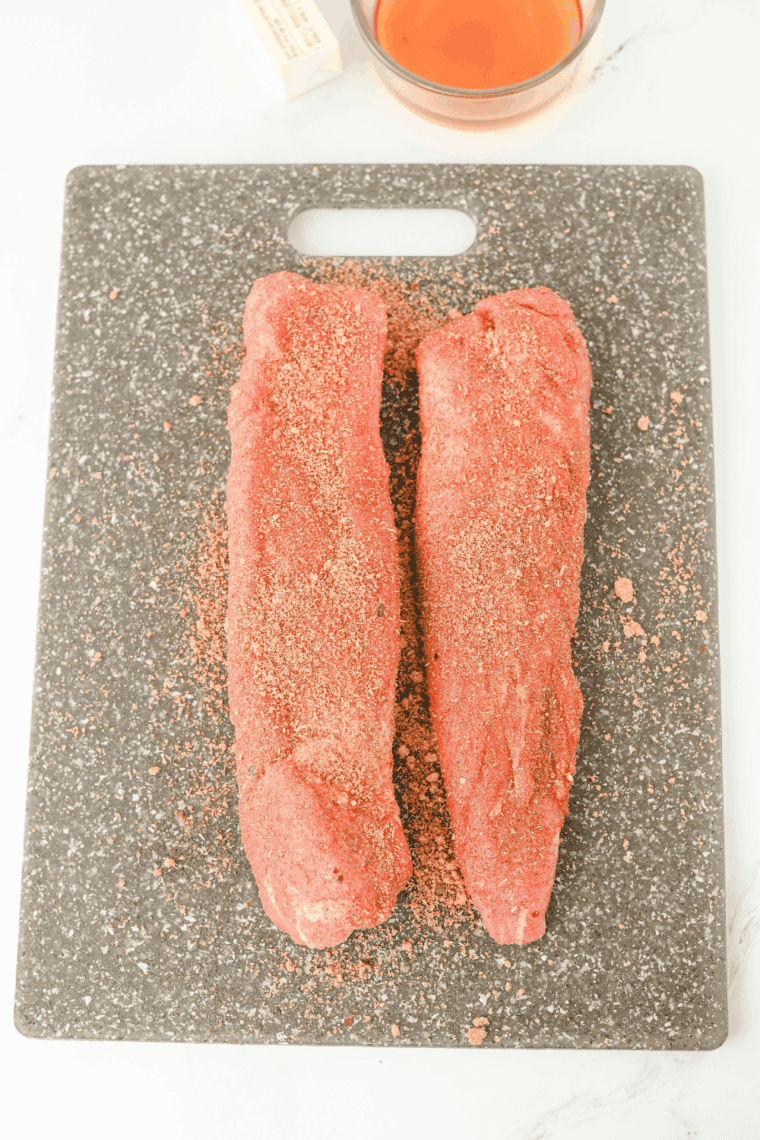 Two pork tenderloins rubbed with a smoked paprika and garlic spice blend on a cutting board