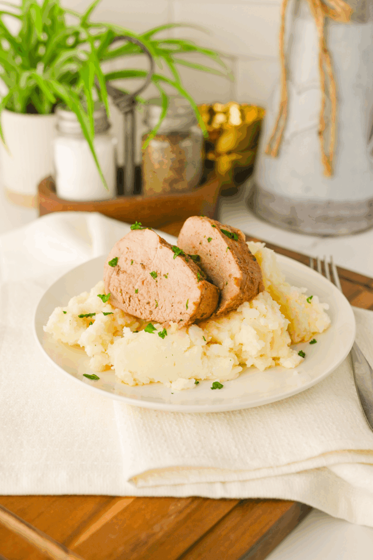 Slow cooker pork tenderloin resting on a wooden cutting board before slicing against the grain