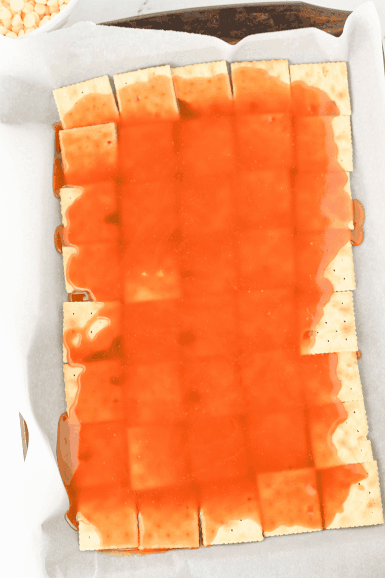 Pouring caramel evenly over saltine crackers on pan
