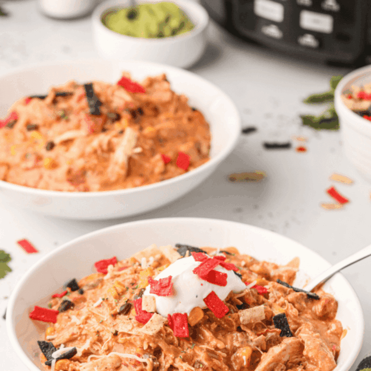 Bowl of creamy white chicken chili topped with cheese and fresh herbs.