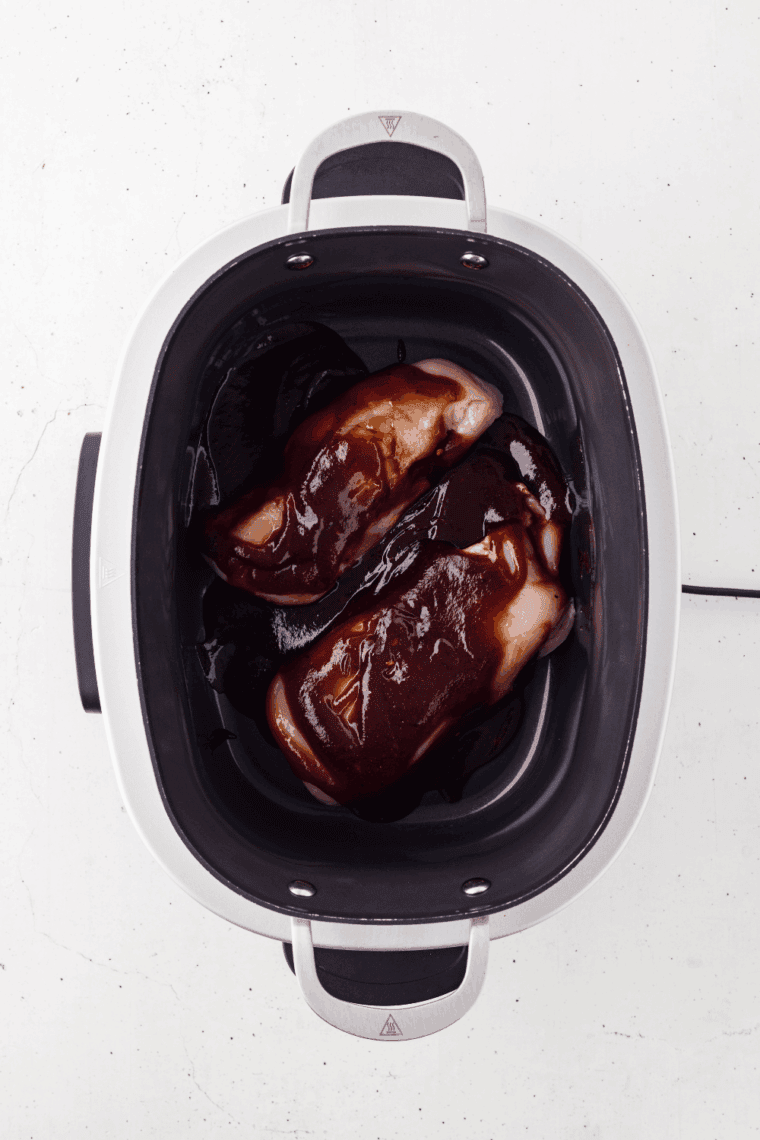 Pouring Sweet Baby Ray’s BBQ sauce over chicken, coating each piece evenly.