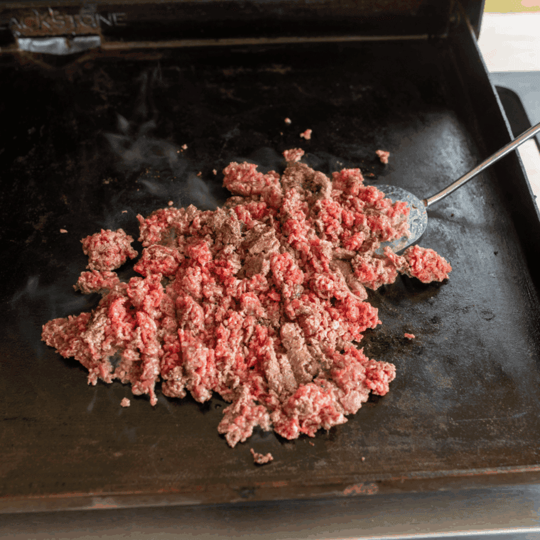 Chopped onions and garlic sautéing in olive oil on a preheated Blackstone griddle
