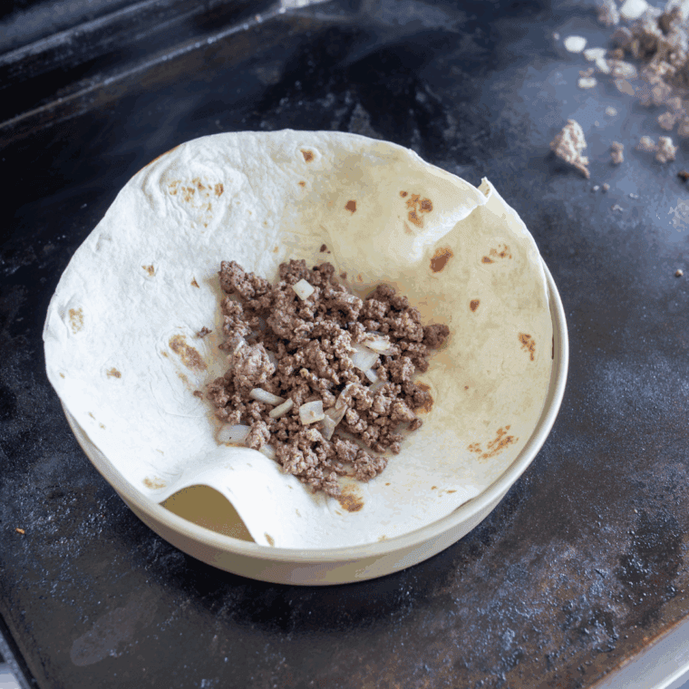 Chili powder, cumin, and paprika sprinkled over browned beef on the griddle