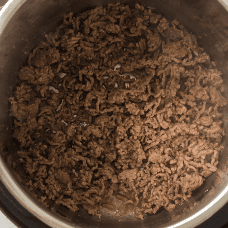 A wooden spoon scraping the bottom of an Instant Pot with beef broth to remove flavorful browned bits.