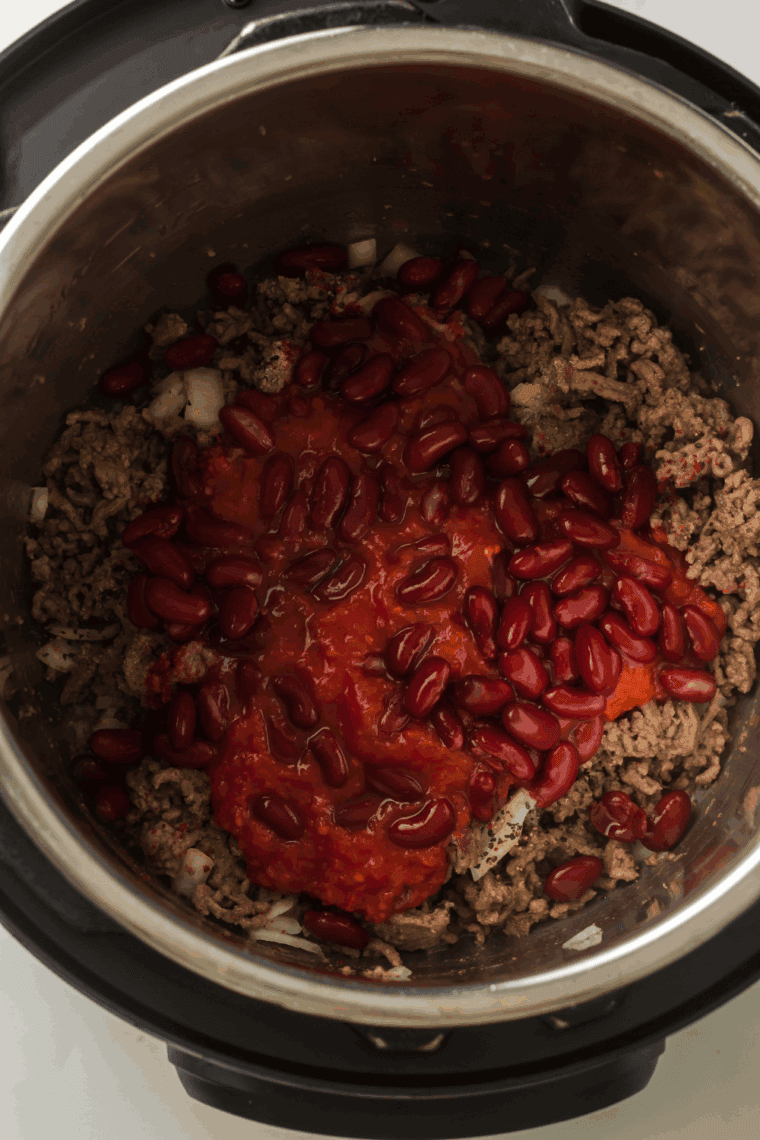 Red kidney beans, tomato sauce, and spices layered inside an Instant Pot before being stirred or cooked.