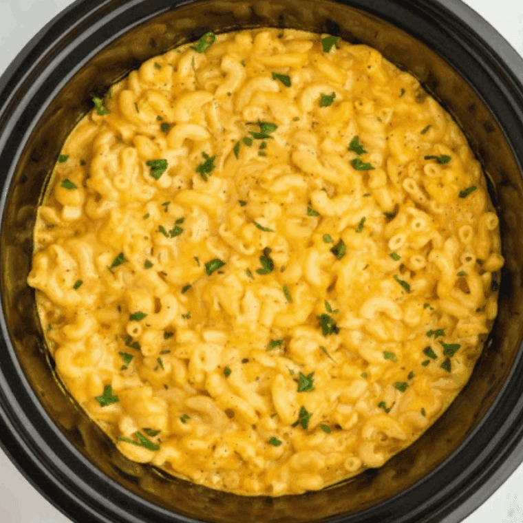 Top-down view of creamy, golden Bojangles mac and cheese in a black slow cooker with parsley garnish.