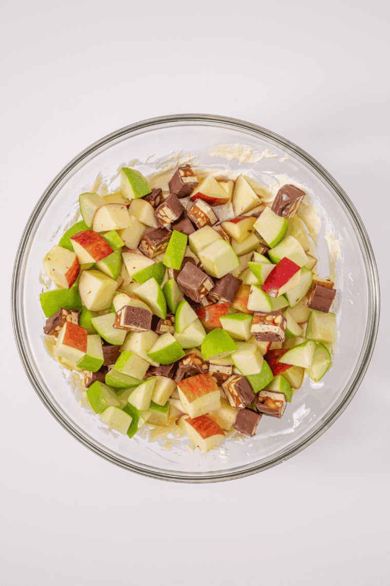 Diced apples and chopped Snickers being folded into the creamy pudding and Cool Whip dressing