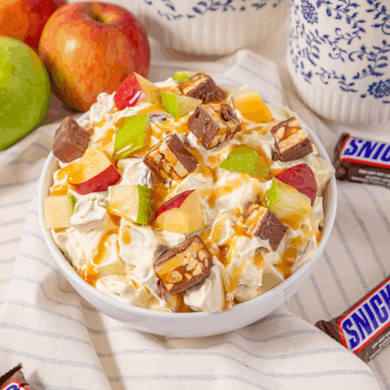 Candy bar apple salad in a white bowl with diced green and red apples, Snickers chunks, and caramel drizzle