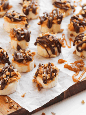 Frozen banana bites topped with chopped Snickers and drizzled chocolate, served on a plate
