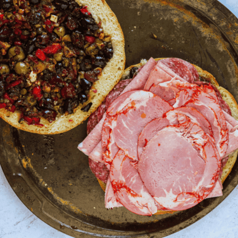 Layers of thinly sliced ham, Genoa salami, and white provolone cheese piled high on a round loaf of bread.