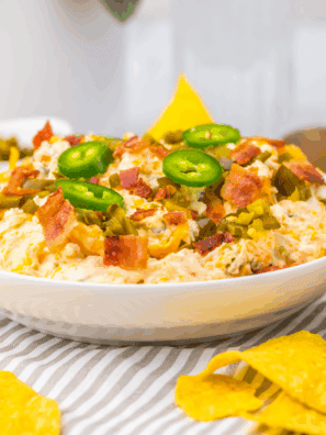 Slow cooker jalapeño popper dip with cream cheese, melted cheddar, bacon, and sliced jalapeños in a crockpot