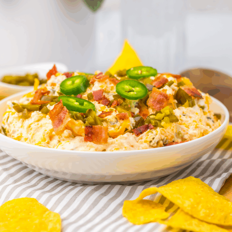 Slow cooker jalapeño popper dip with cream cheese, melted cheddar, bacon, and sliced jalapeños in a crockpot