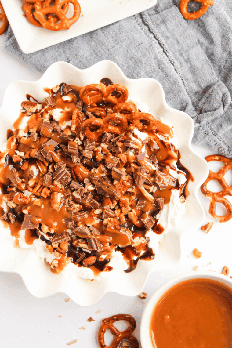 Bowl of Easy Turtle Cheesecake Dip topped with chocolate drizzle, caramel, and chopped pecans, ready for serving with crackers or fruit.